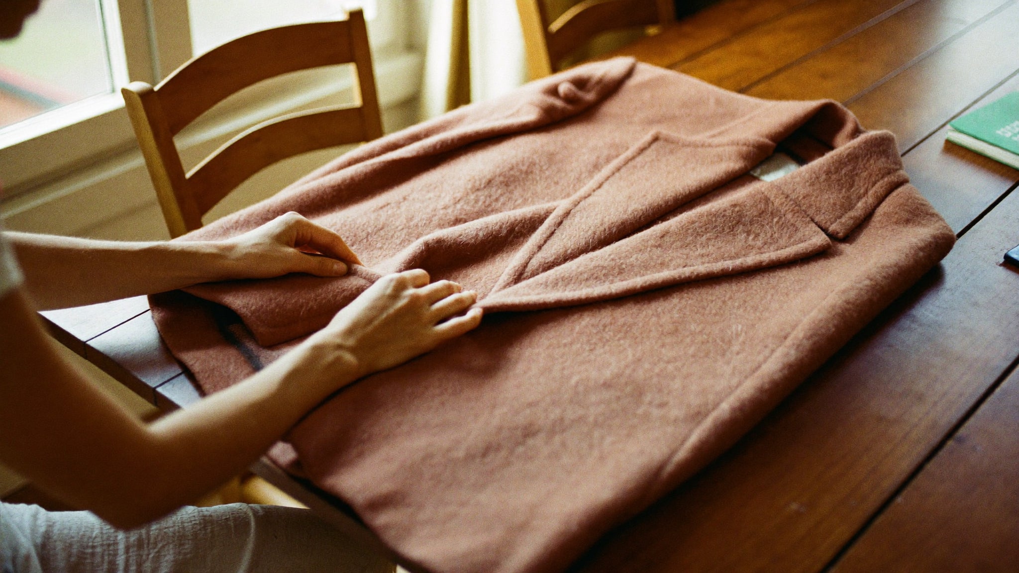 Hands carefully folding a camel wool coat